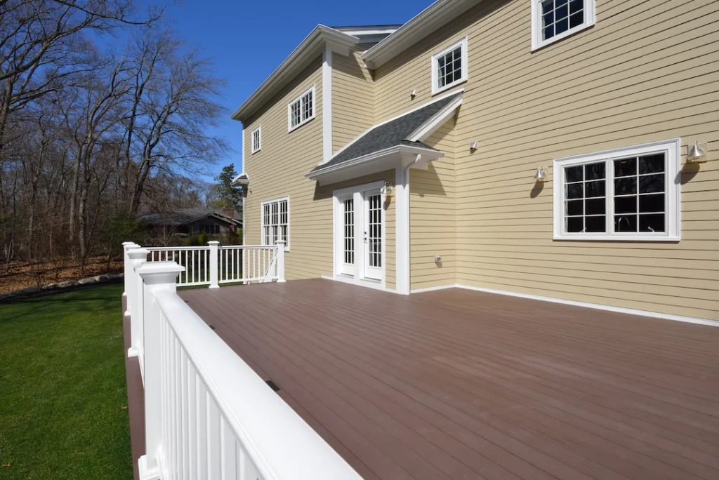 Composite deck in house backyard. Brown boards, white railing posts and veranda. Large, spacious, new construction.
