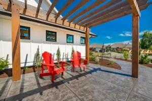 bright and sunny patio with pergola stamped concrete with two red Adirondack chairs deep and beautiful blue sky bark mulch new landscaping a backdrop of a white home with windows reflecting the sky